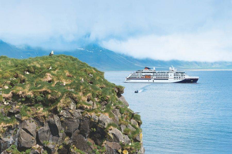Hapag-Lloyd Cruises Kreuzfahrtschiff vor der grünen und felsigen Küste Islands
