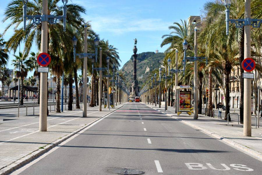 Eine leere, von Palmen gesäumte Straße führt direkt zur berühmten Kolumbus-Statue in Barcelona, mit dem Montjuïc-Berg im Hintergrund.