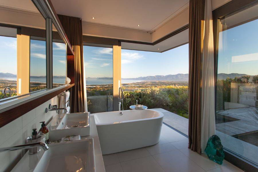 Luxus-Badezimmer mit freistehender Badewanne, modernen Waschbecken und raumhohen Fenstern mit Blick auf die malerische Landschaft.