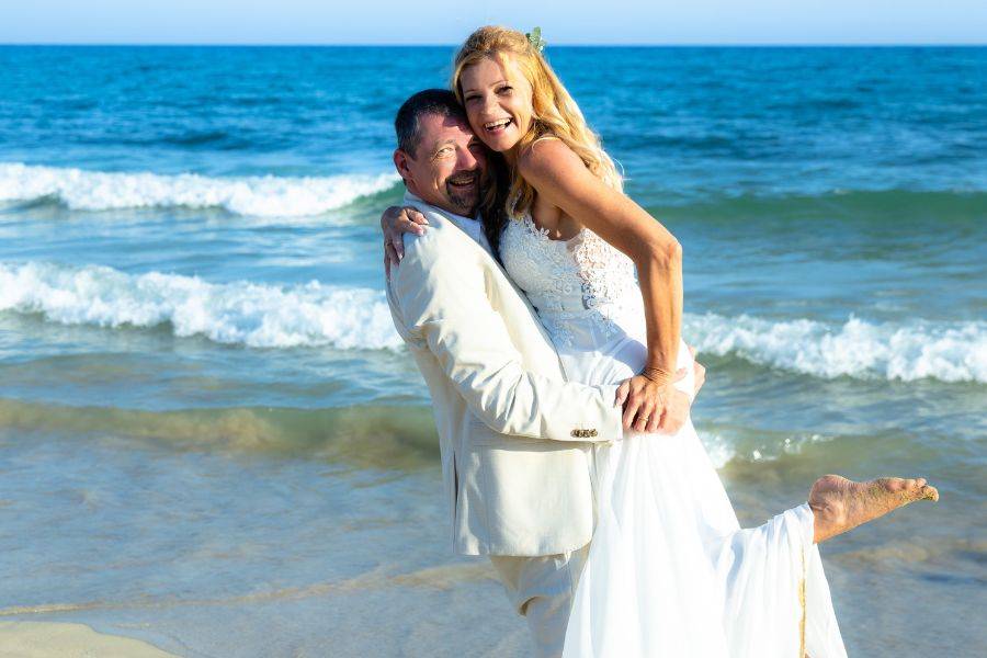 Hochzeitspaar am Strand. Bräutigam trägt seine Braut im Arm