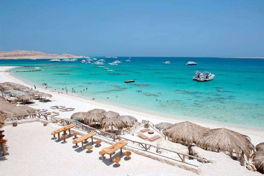 Weißer Sandstrand auf Giftun Island bei Hurghada mit Blick auf das türkisfarbene Meer und Ausflugsboote im Hintergrund.