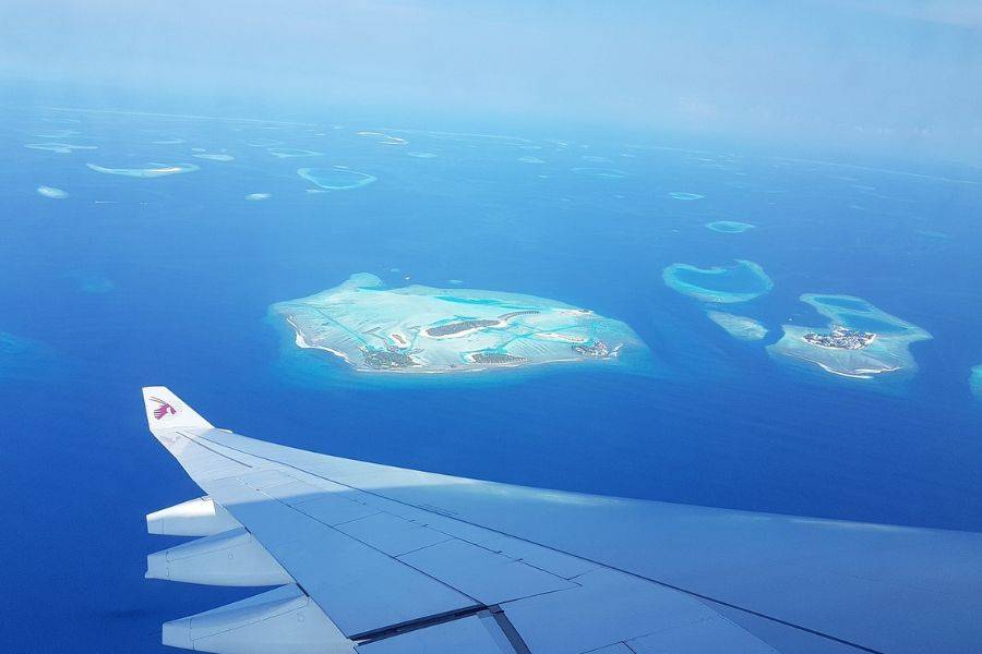Ein atemberaubender Blick aus dem Fenster eines Flugzeugs auf die türkisblaue Lagune und die paradiesischen Inseln der Malediven. Die Tragfläche des Flugzeugs ragt ins Bild und unterstreicht das Gefühl einer bevorstehenden Traumreise zu den exotischen Atollen.