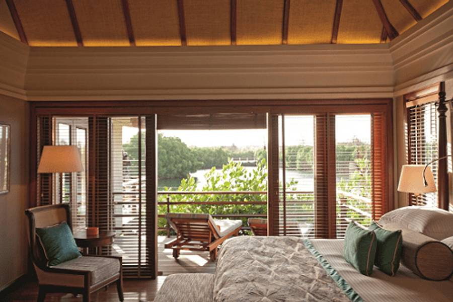 Innenansicht eines eleganten Hotelzimmers mit Bett, Sesseln und einem Balkon mit Blick auf tropisches Grün.