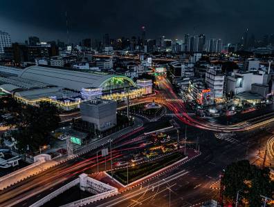 Ein nächtliches Stadtpanorama mit beleuchteten Straßen und einem modernen Bahnhof im Vordergrund, während Lichtspuren von Fahrzeugen Bewegung andeuten und die Skyline der Stadt im Hintergrund sichtbar ist.