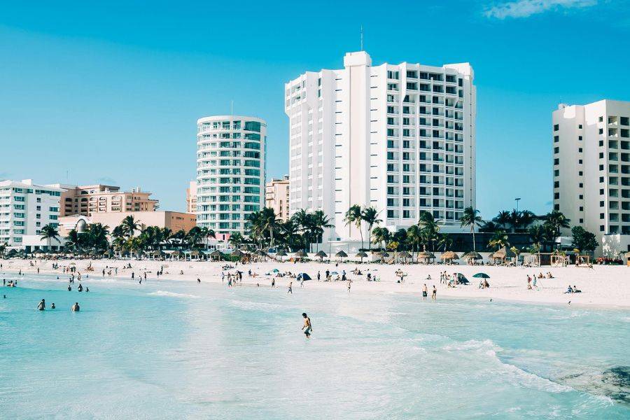 Weißer Sandstrand mit türkisblauem Wasser vor modernen Hotelbauten in Cancún, Mexiko.