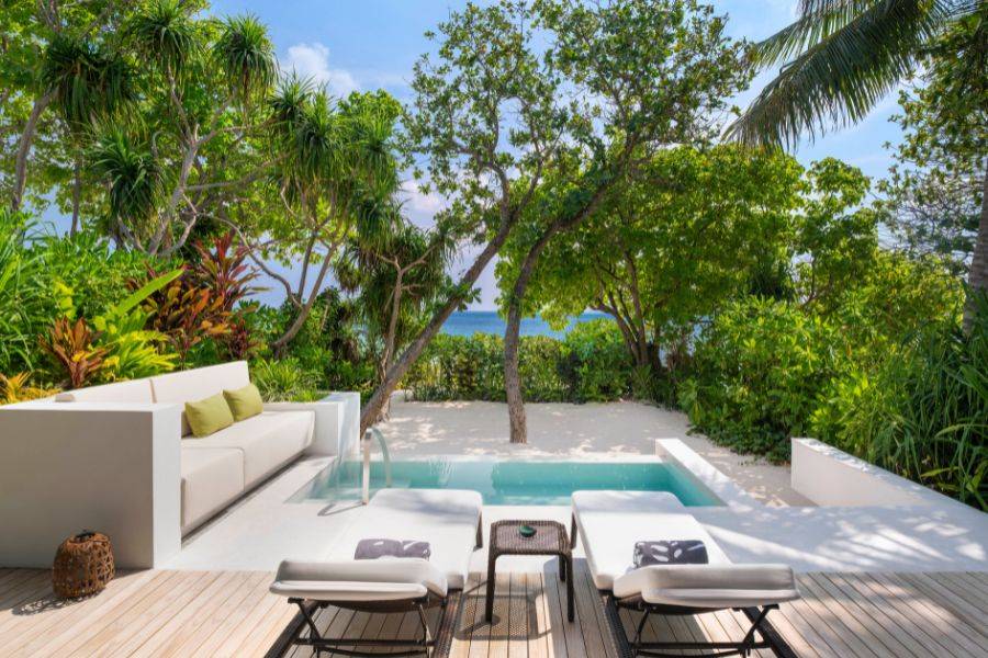 Private Terrasse mit Sonnenliegen, Pool und Sofa, umgeben von tropischer Vegetation mit Blick auf das Meer.