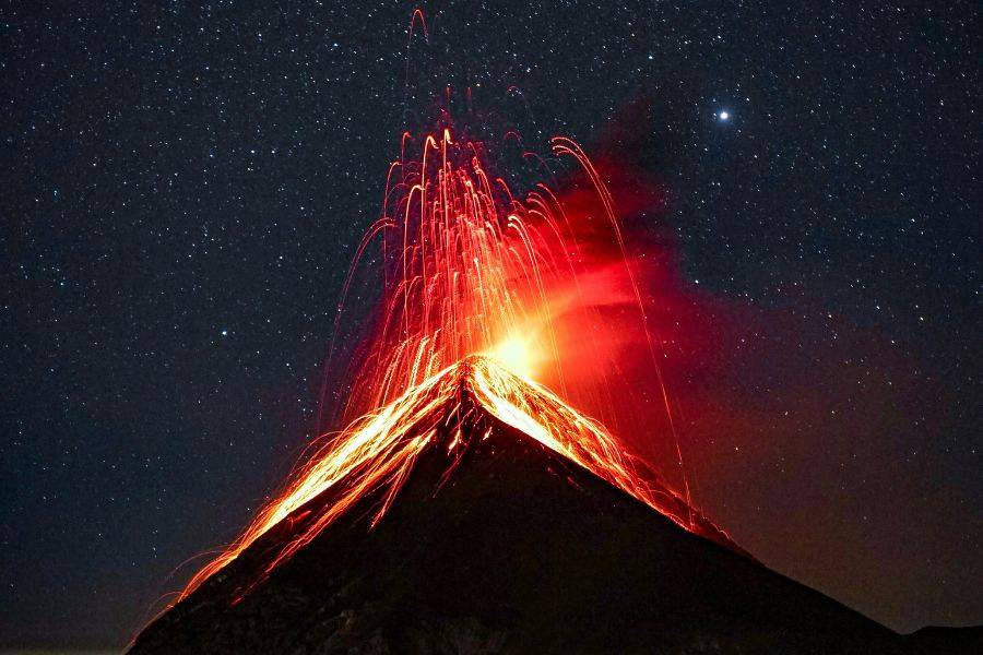 Spektakuläre nächtliche Aufnahme des ausbrechenden Vulkans Fuego in Guatemala mit leuchtender Lava unter einem klaren Sternenhimmel – ein unvergessliches Naturschauspiel.