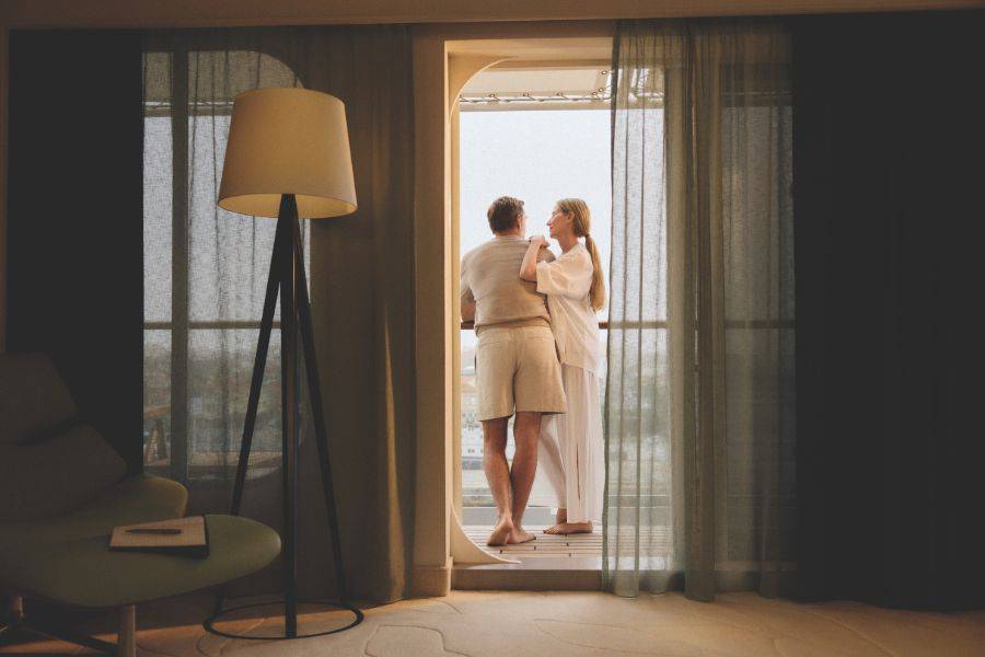 Paar steht auf dem Balkon einer Schiffskabine und blickt gemeinsam auf das Meer im warmen Morgenlicht