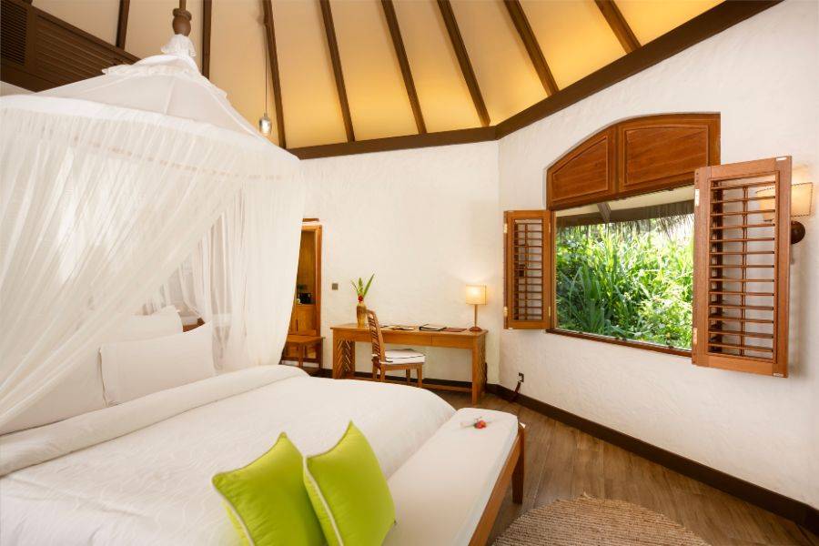 Gemütliches Schlafzimmer mit Himmelbett und Schreibtisch, offenem Fenster mit Blick ins Grüne, in einer tropischen Villa mit traditionellem Holzdesign.