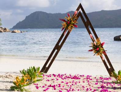 Tropisch dekorierter Traubogen für eine Strandhochzeit im Raffles Praslin Resort auf den Seychellen – exklusive Hochzeitslocation direkt am Indischen Ozean.