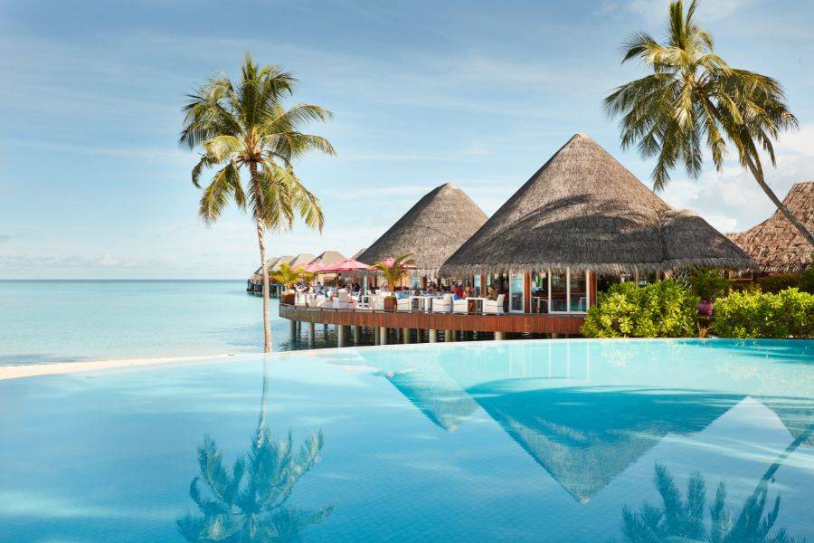 Ein Infinity Pool endet in einer aussicht auf das offene Meer und den Strand. Daneben sieht man einen Bungalow, in welchem das Restaurant des Resorts ist.