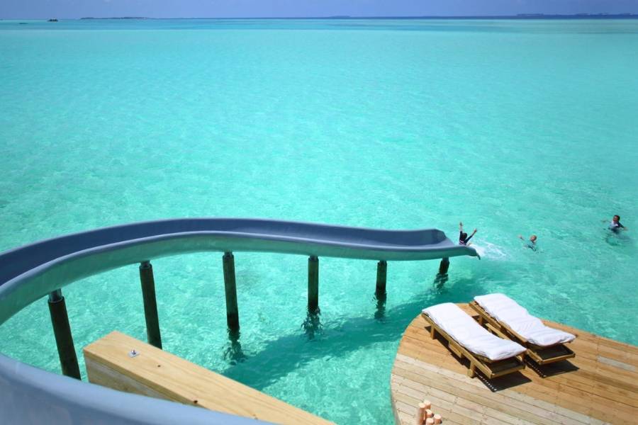 Geschwungene Wasserrutsche in die türkisfarbene Lagune neben einer Holzterrasse mit zwei Sonnenliegen