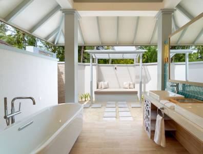 Elegantes, halb offenes Badezimmer mit freistehender Badewanne, Doppelwaschtisch und Lounge-Bereich im Freien, umgeben von tropischer Vegetation.