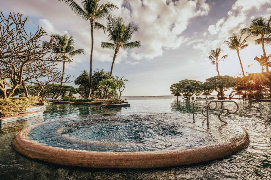 Ausblick auf einen modernen Infinity Pool.  Daneben sieht man eine Palmenlandschaft.