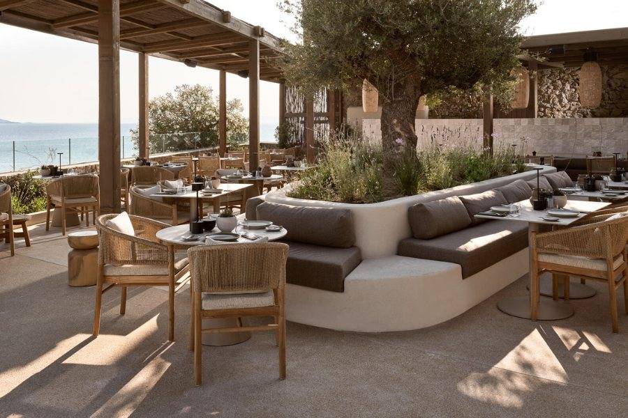 Gemütlicher Außenbereich eines Restaurants mit Meerblick, Holzmöbeln und mediterraner Atmosphäre.
