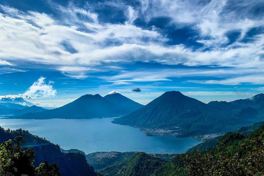 Panoramablick auf den Atitlán-See in Guatemala, umgeben von drei majestätischen Vulkanen unter dramatisch bewölktem Himmel – ein beeindruckendes Naturparadies.