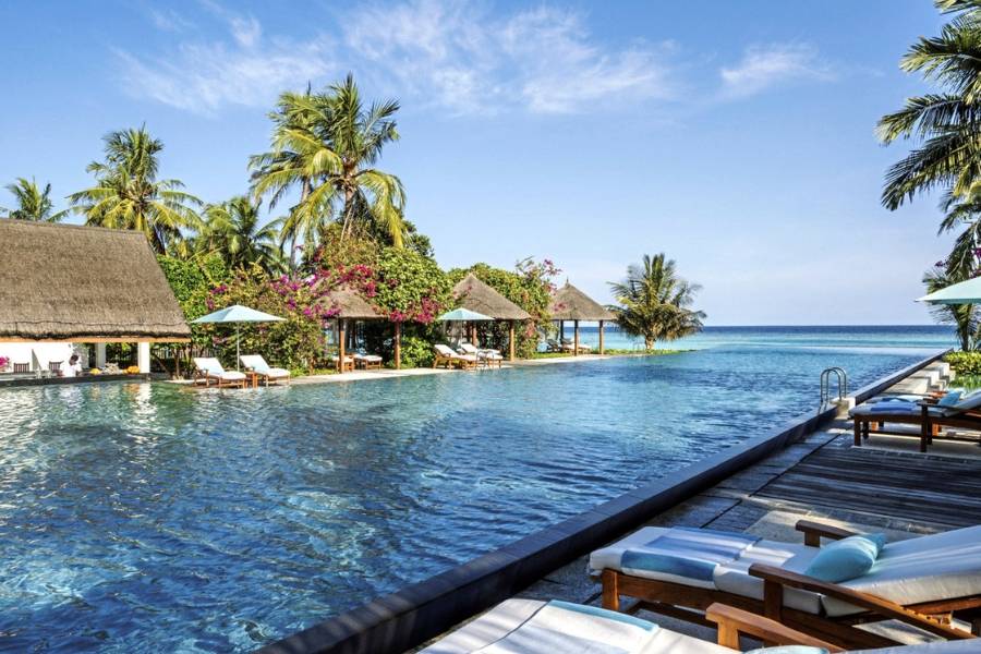 Großer Pool mit Meerblick, umgeben von Sonnenliegen, Palmen und strohgedeckten Pavillions im Four Seasons Landaa Giraavaru.