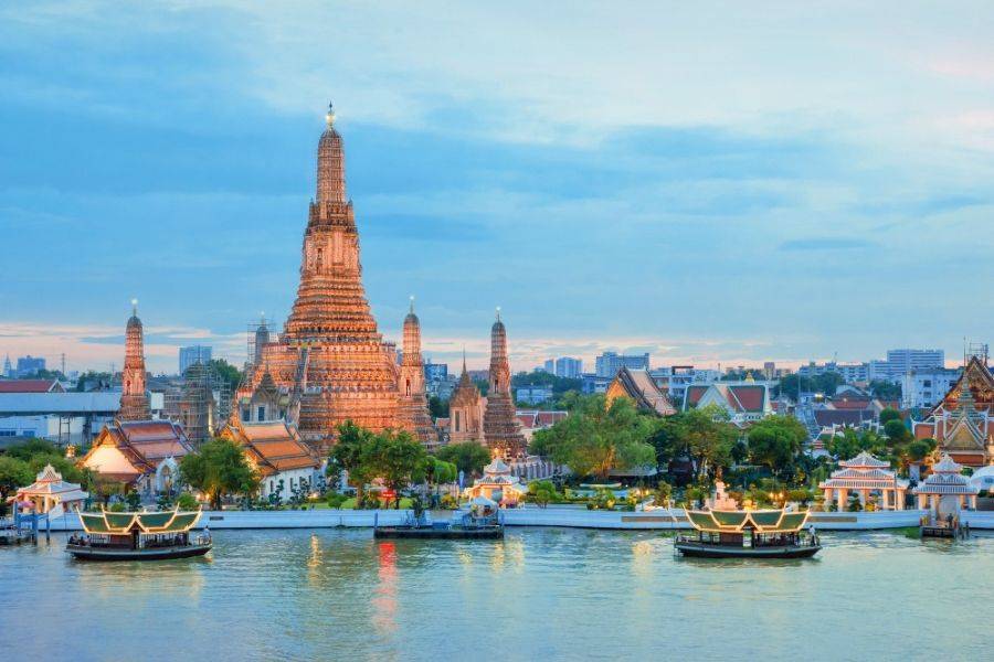 Wat Arun Tempel in Bangkok bei Sonnenuntergang mit beleuchteten Booten auf dem Chao-Phraya-Fluss