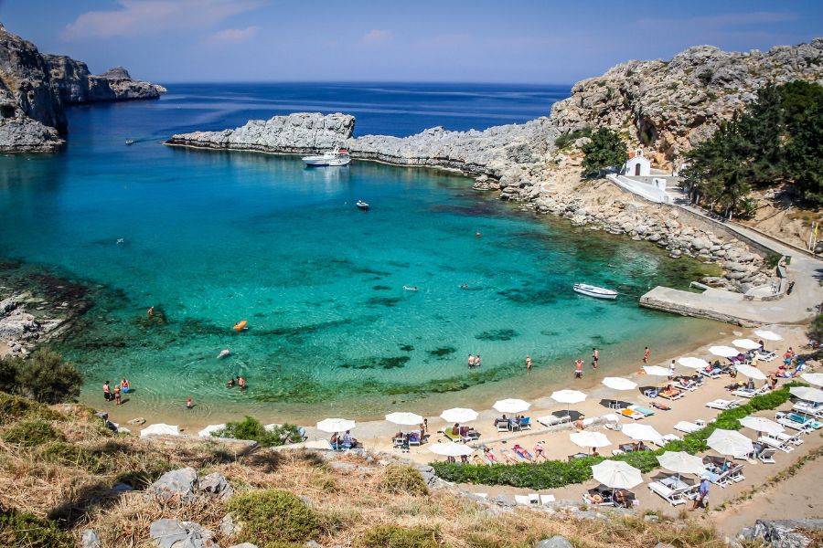 Türkisfarbene Bucht mit Strandliegen und Felsen an der Küste von Rhodos, Griechenland