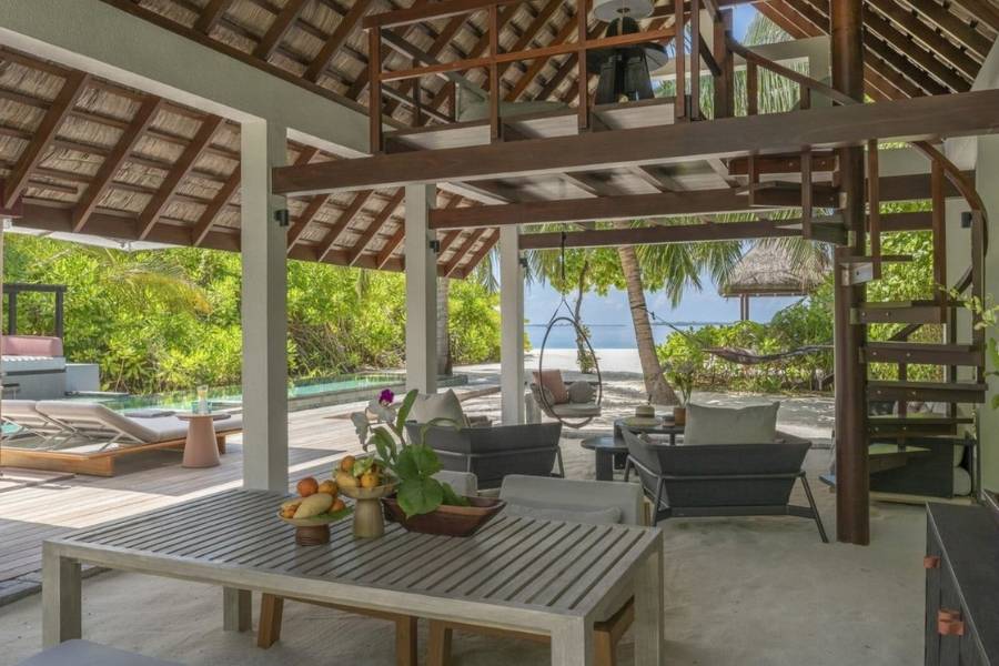 Überdachter Wohn- und Essbereich einer Strandvilla mit Sandboden, Wendeltreppe und Blick auf privaten Pool und das Meer. 