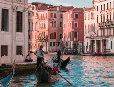 Gondeln mit Passagieren gleiten durch einen kleinen Kanal in Venedig, umgeben von historischen Gebäuden mit typischer venezianischer Architektur.