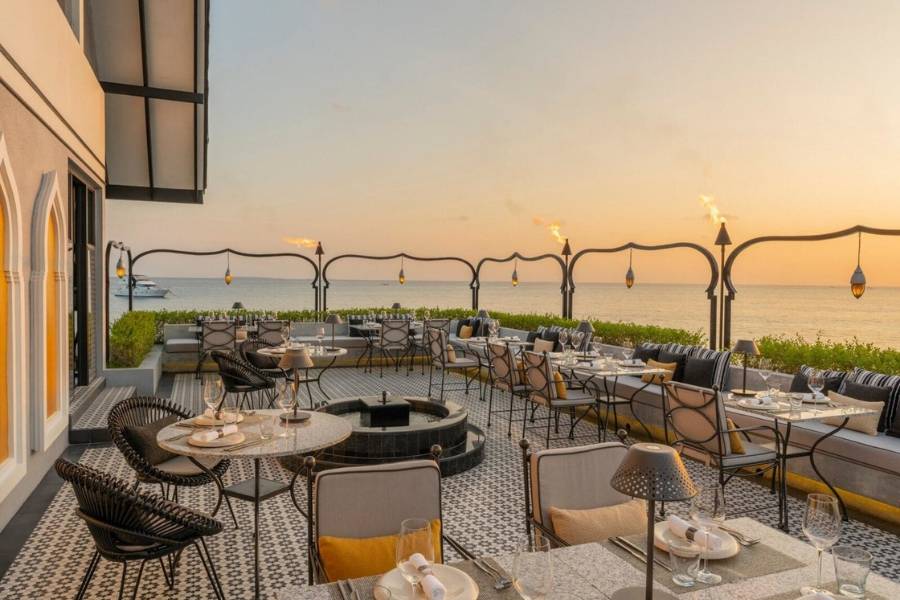 Gedekte Tische auf einer Restaurantterrasse mit Laternen, brennenden Fackeln und Meerblick mit Sonnenuntergang.