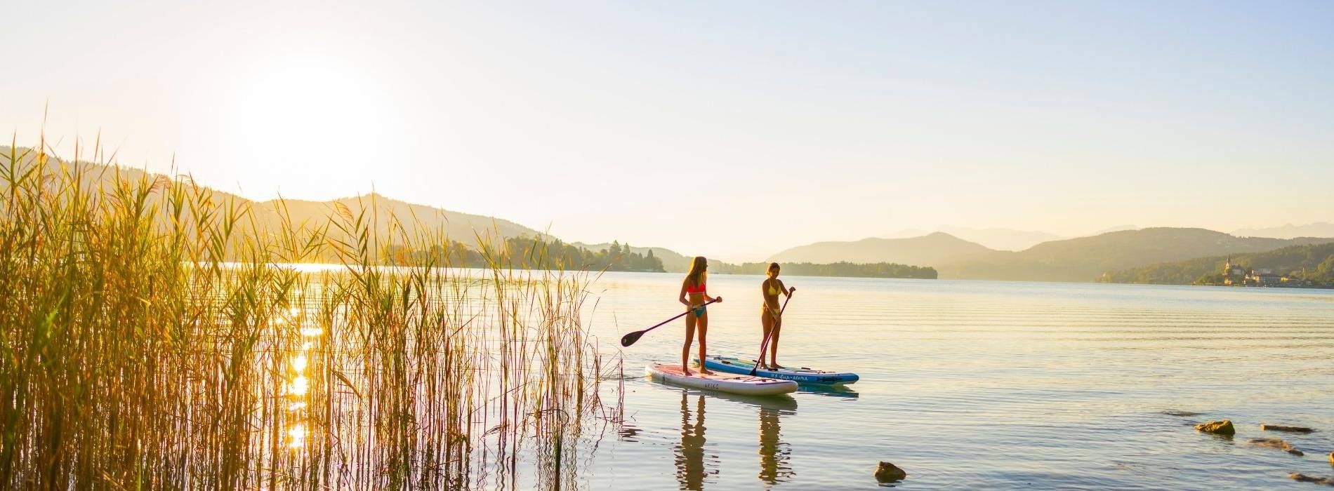 Zwei Frauen beim Stand-Up-Paddling auf einem ruhigen Bergsee bei Sonnenuntergang