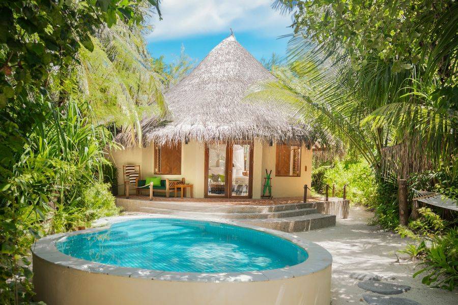 Charmanter tropischer Bungalow mit Strohdach, umgeben von üppigem Grün, mit privatem Rundpool auf weißem Sandboden.