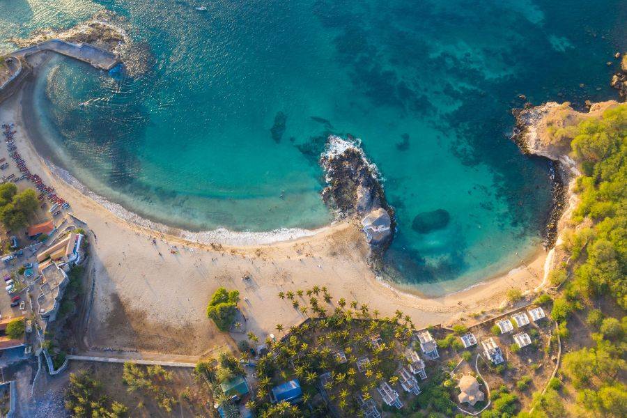 Luftaufnahme einer geschützten Bucht mit türkisfarbenem Wasser, feinem Sandstrand und Palmen auf der Kapverdischen Insel.