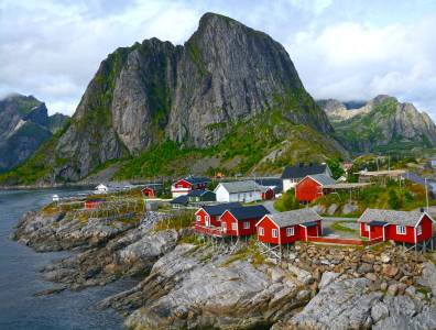 Rote Fischerhütten auf den Lofoten vor steilen Bergen und fjordreicher Küstenlandschaft in Norwegen