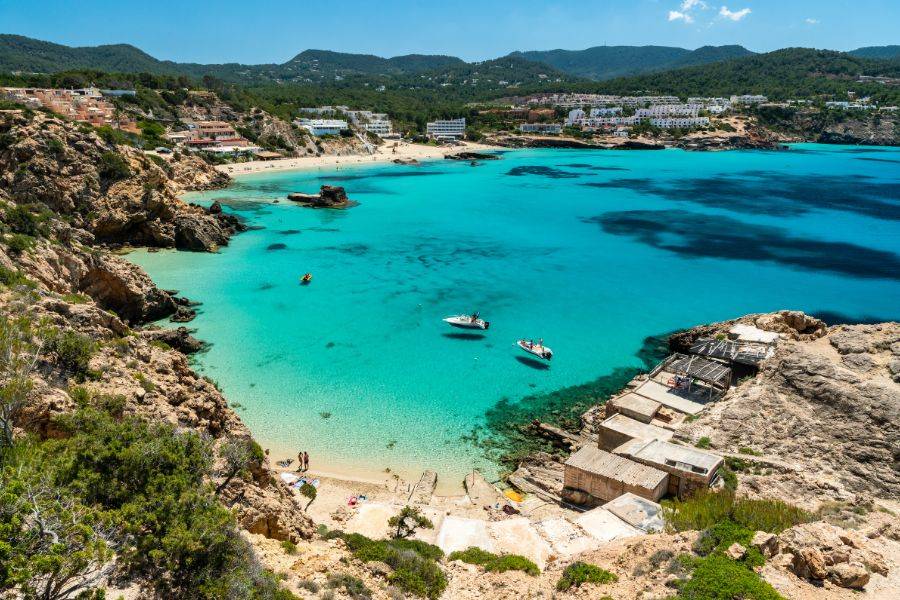 Türkisfarbene Bucht auf Ibiza mit Sandstrand, Felsküste und kleinen Booten
