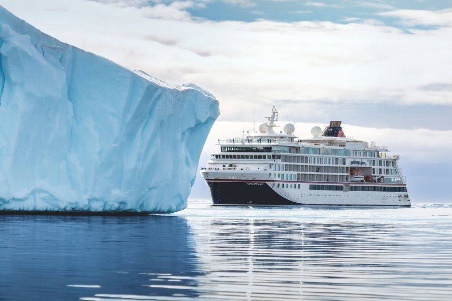 Expeditionsschiff von Hapag-Lloyd Cruises fährt an einem großen Eisberg in polaren Gewässern vorbei