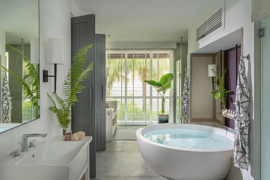  Stilvolles Badezimmer mit runder freistehender Badewanne, tropischer Bepflanzung und großen Fensterfronten mit Blick ins Grüne.