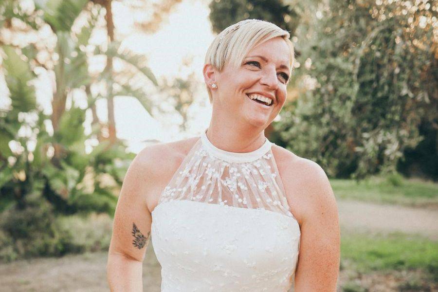 Porträt einer lächelnden Braut im eleganten Hochzeitskleid, aufgenommen im weichen Licht vor grünem Hintergrund auf einer griechischen Insel.