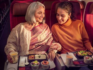 Zwei Passagierinnen genießen eine warme Mahlzeit an Bord von Air India in der Economy Class und lächeln einander an.