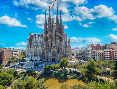 Die weltberühmte Basilika von Antoni Gaudí mit ihren hoch aufragenden Türmen und detailreichen Fassaden, vor einem strahlend blauen Himmel.