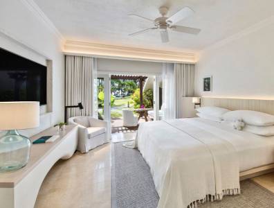 Lichtdurchflutetes Hotelzimmer in hellen Naturtönen mit großem Bett, Deckenventilator, modernem Interieur und Zugang zur Terrasse mit Blick ins Grüne.