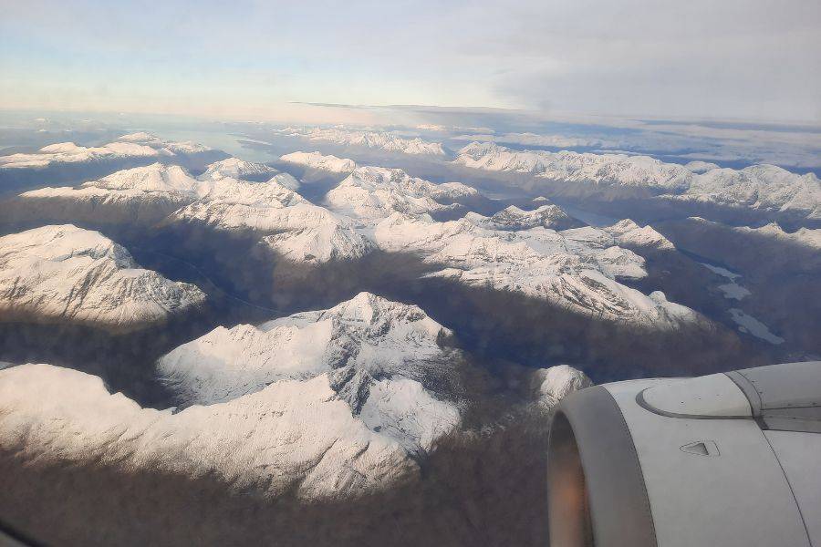 Blick aus einem Flugzeugfenster auf eine beeindruckende Landschaft mit schneebedeckten Bergen, die sich bis zum Horizont erstrecken, unter einem klaren Himmel.