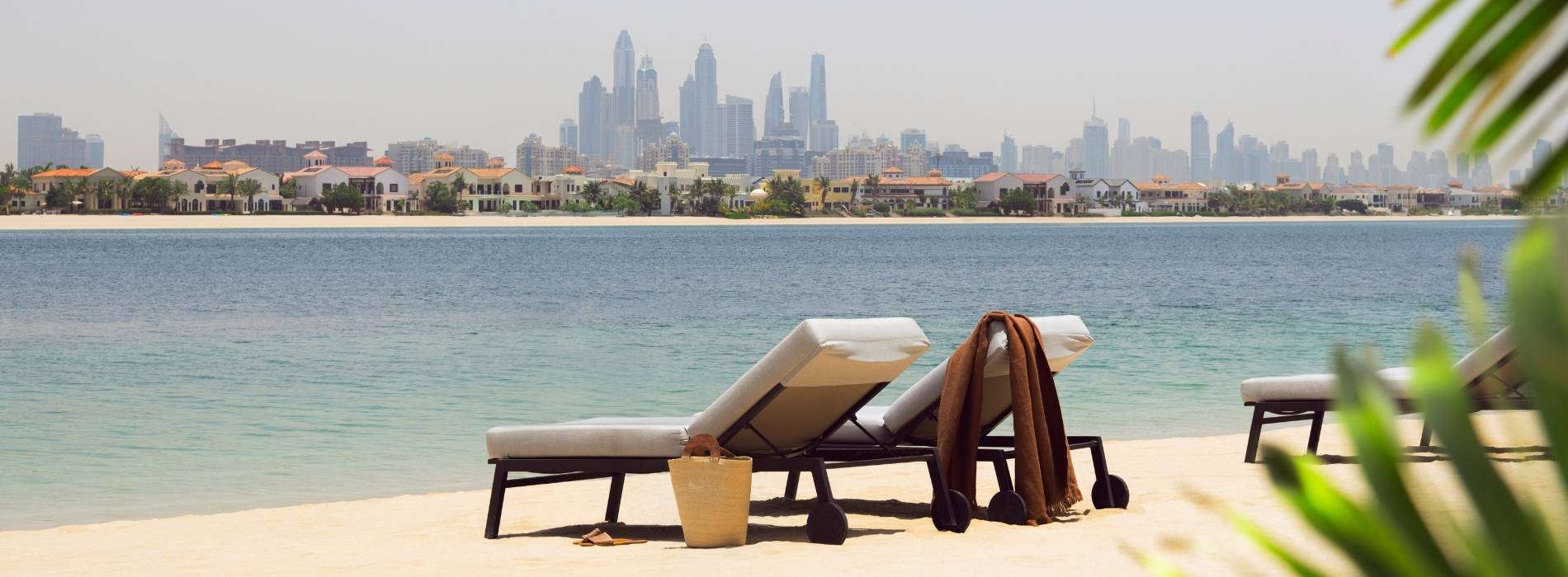 Liegestühle am Strand mit Blick auf die Skyline von Dubai über das Meer hinweg