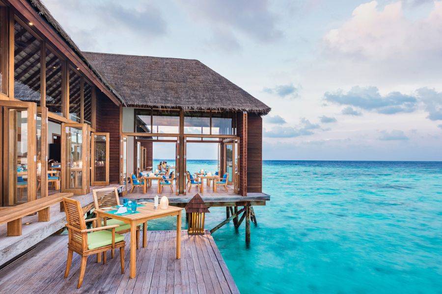 Offenes Restaurant auf Stelzen direkt über türkisblauem Meer, mit Holzmöbeln und weitem Blick auf den Ozean.