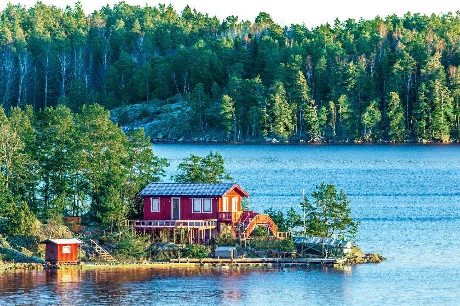 Rotes Holzhaus an einem bewaldeten See in Schweden
