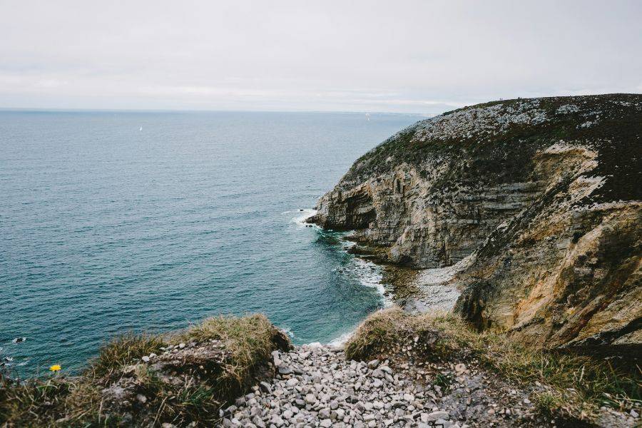 Felsküste an der Pointe du Raz in der Bretagne, mit einem Pfad im Vordergrund und weitem Blick auf den Atlantik.