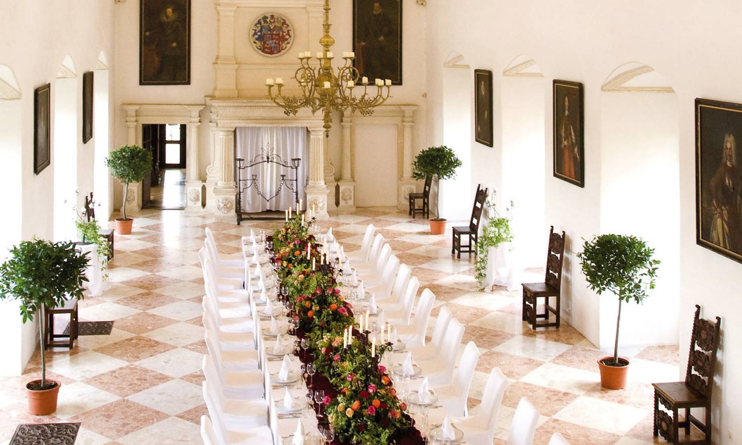 Ein eleganter Saal mit gewölbter Decke, einem langen, festlich gedeckten Tisch, weißen Stühlen und Kronleuchtern.