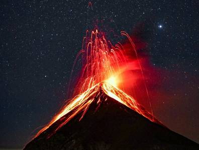 Spektakuläre nächtliche Aufnahme des ausbrechenden Vulkans Fuego in Guatemala mit leuchtender Lava unter einem klaren Sternenhimmel – ein unvergessliches Naturschauspiel.