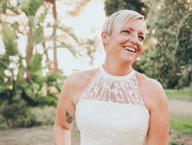 Porträt einer lächelnden Braut im eleganten Hochzeitskleid, aufgenommen im weichen Licht vor grünem Hintergrund auf einer griechischen Insel.