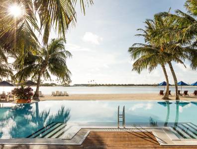 Moderner Poolbereich mit Einstiegstreppe und Meerblick, eingerahmt von Palmen und Sonnenliegen, mit Blick auf einen ruhigen, tropischen Strand.