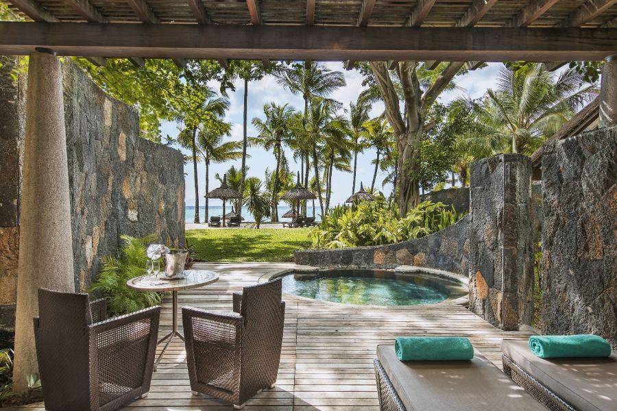 Private Terrasse mit kleinem Pool, zwei Sonnenliegen und einem Sitzbereich mit Blick auf Palmen, Rasenfläche und das Meer in tropischer Umgebung.