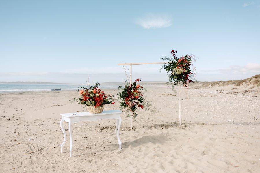 Ein hübsch gedeckter Hochzeitstisch und ein Hochzeitsbogen am Strand.