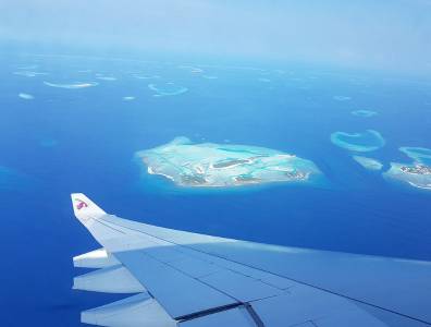 Ein atemberaubender Blick aus dem Fenster eines Flugzeugs auf die türkisblaue Lagune und die paradiesischen Inseln der Malediven. Die Tragfläche des Flugzeugs ragt ins Bild und unterstreicht das Gefühl einer bevorstehenden Traumreise zu den exotischen Atollen.