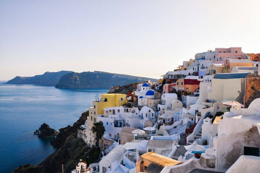 Atemberaubender Blick über die Küste von Santorini mit farbenfrohen Häusern auf der Klippe und der tiefblauen Ägäis im Hintergrund.